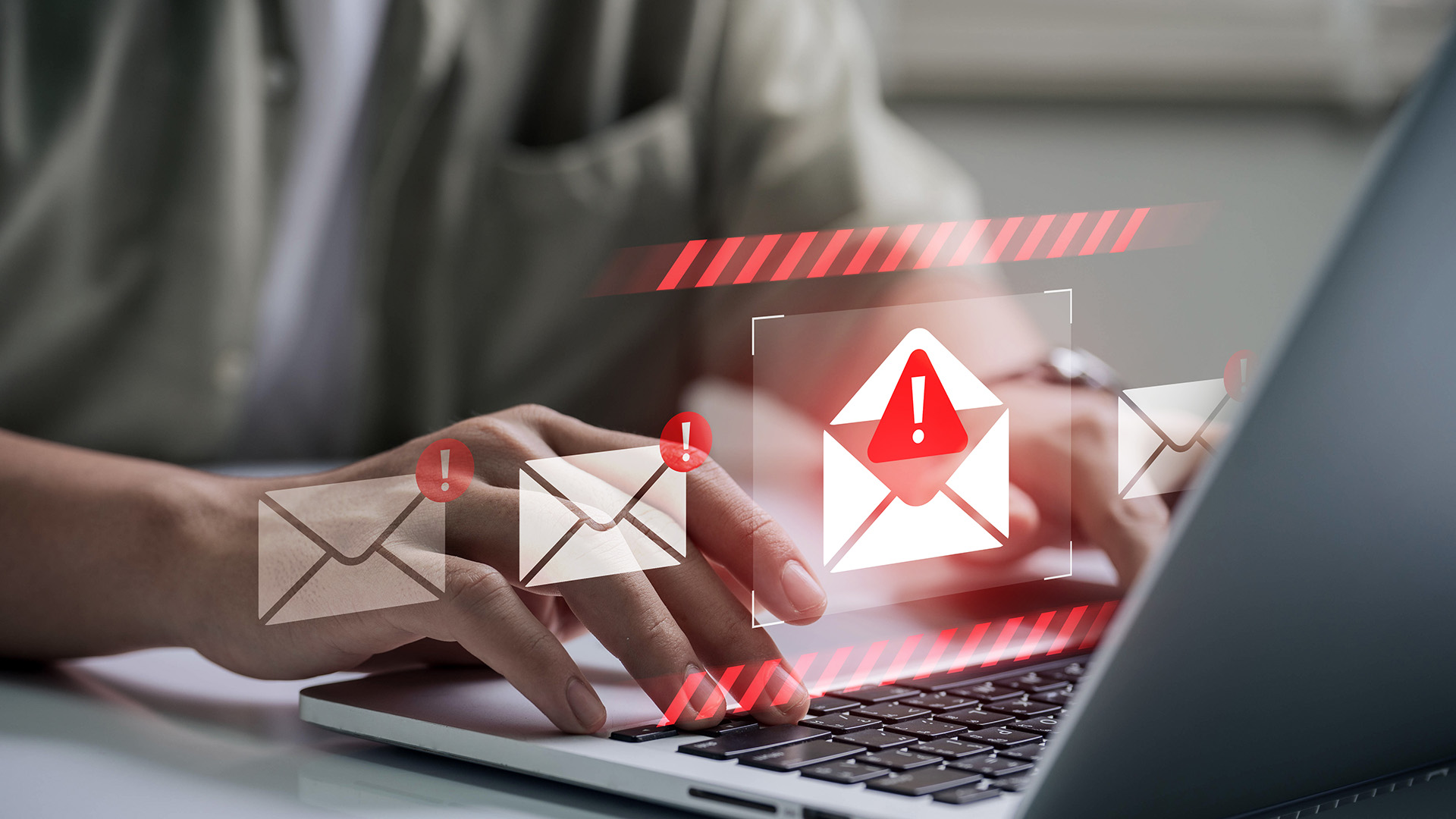 Hands typing on a laptop with envelope icons and red exclamation marks—phishing email warning.