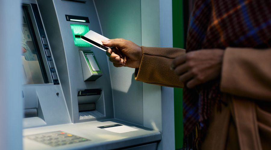 Person inserting a debit card into an ATM—reminder to check for skimmers and cover the keypad.
