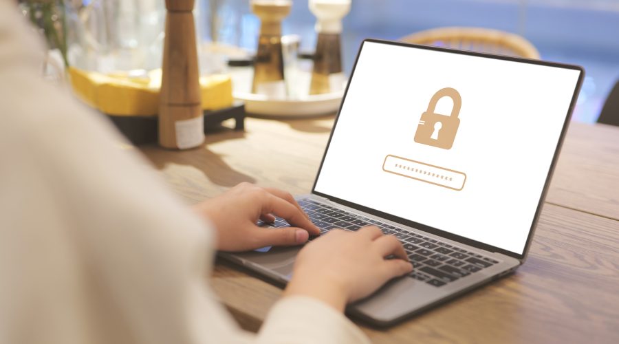 Person on café Wi-Fi using a laptop; screen shows a padlock and password field—secure login on public networks.