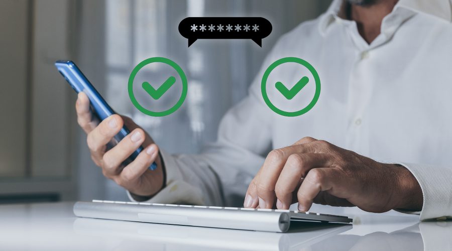 Hands using a phone and keyboard with a password bubble and two green check marks—two-factor authentication login.