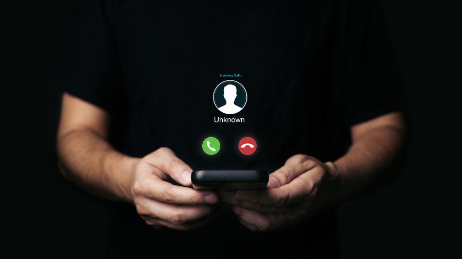 Person holding a smartphone with an “Unknown” incoming call screen—illustrating a phone scam (vishing) warning.