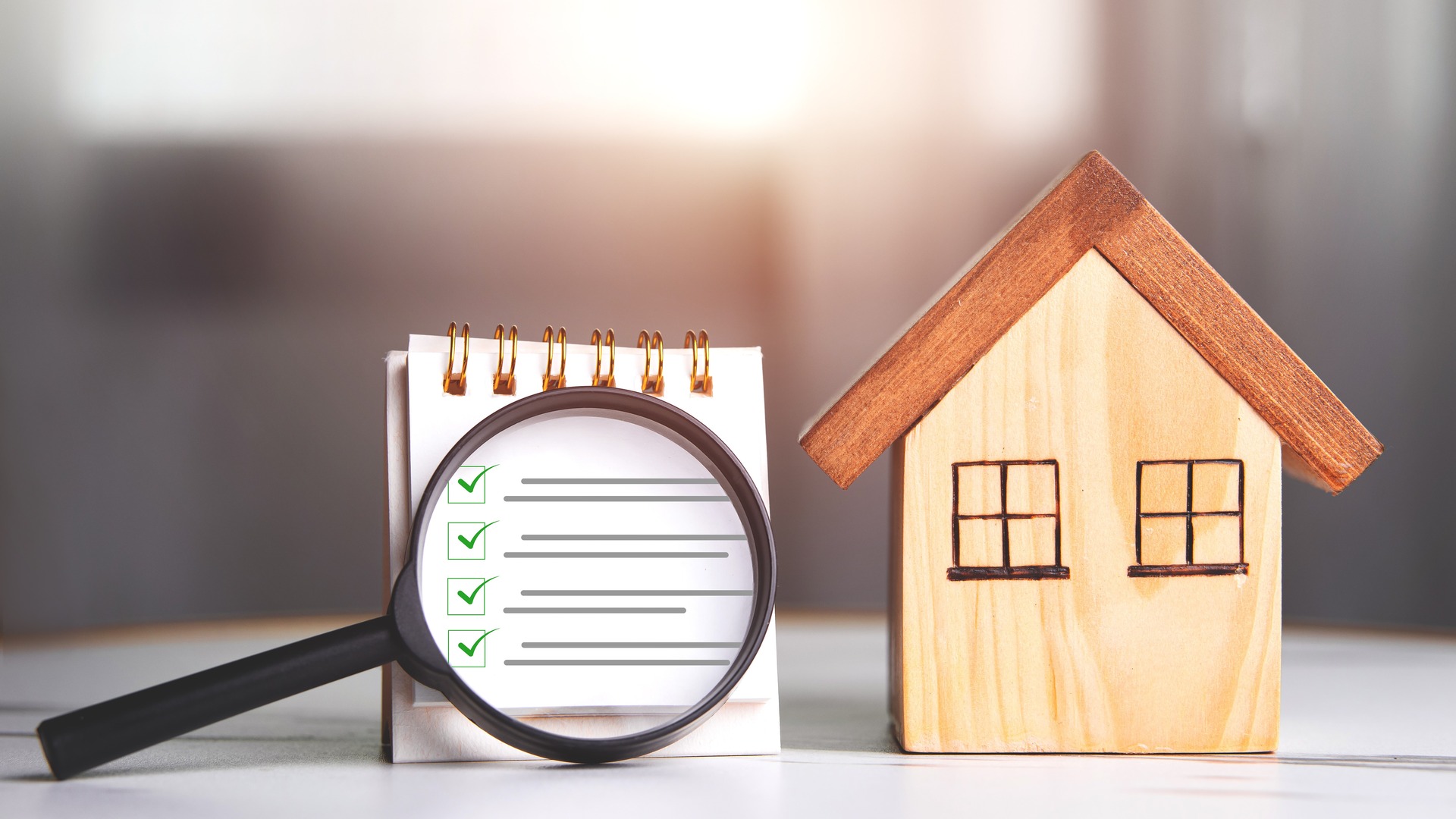 Home buying checklist graphic with a magnifying glass and wooden house model on a notepad.